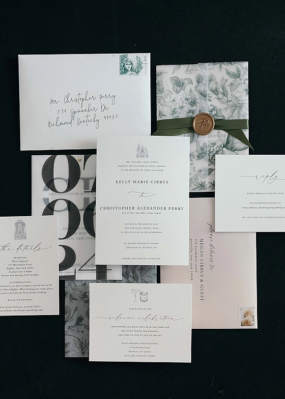 Invitation suite wedding invitation flat lay with black and white cards, vellum wrap, wax seal, and addressed envelope on black fabric backdrop