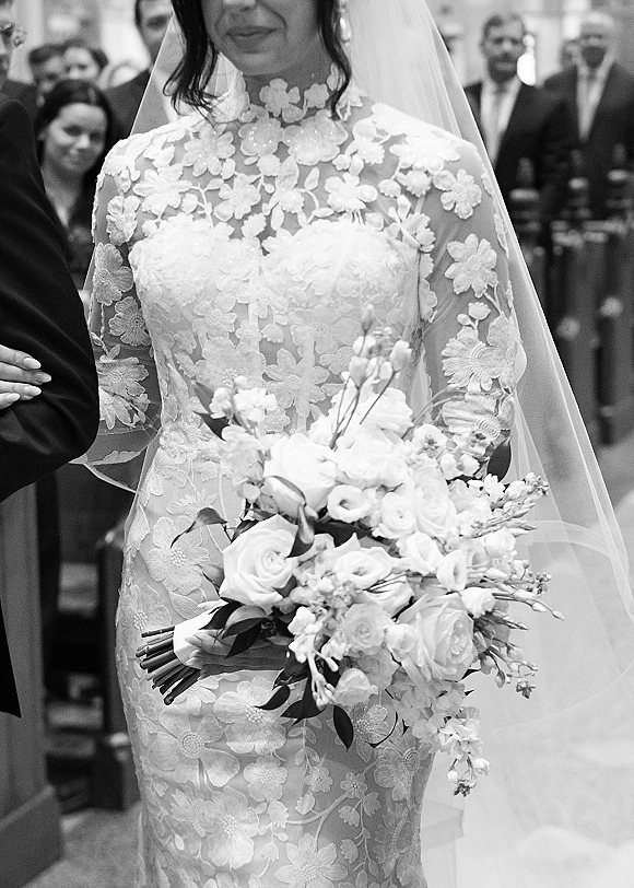Bride portrait in a black and white wedding portrait, holding a rose bouquet in a long sleeve lace dress while walking down the indoor aisle