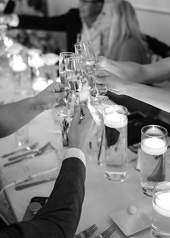 Wedding toast with champagne toast wedding as guests clink champagne flutes and wine glasses over floating candle centerpieces at reception table