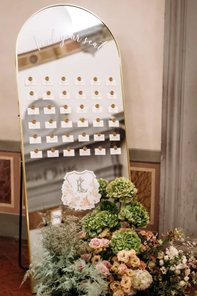Wedding seating chart mirror seating chart on an arched gold frame with wax-sealed escort cards and hydrangea florals by marble wall