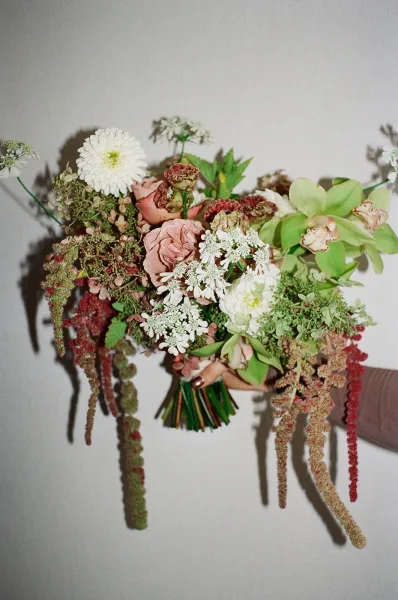 Bridal bouquet, garden style bouquet with roses, dahlias and orchids, accented by hanging amaranthus and greenery against a neutral wall shadow