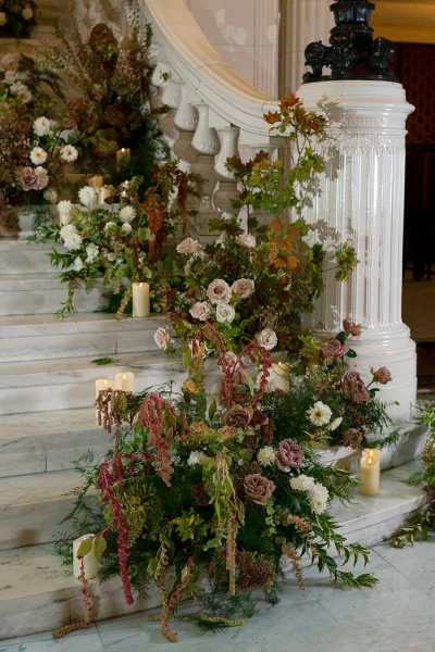 Ceremony staircase florals with a staircase wedding flower installation of roses, dahlias, and greenery garland on a marble stair with candles