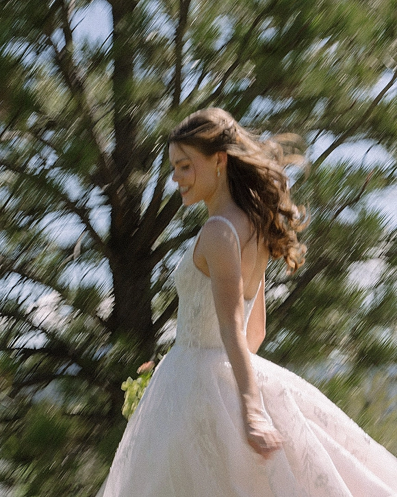 Bridal portrait of a bride in an outdoor bridal portrait, twirling a lace tulle gown with bouquet and drop earrings beneath trees