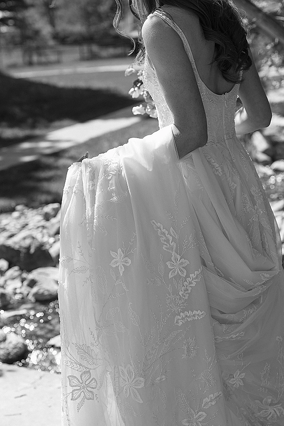 Wedding dress with lace wedding dress detailing, spaghetti straps and low back, tulle skirt and train on a stone path by a creek in a garden