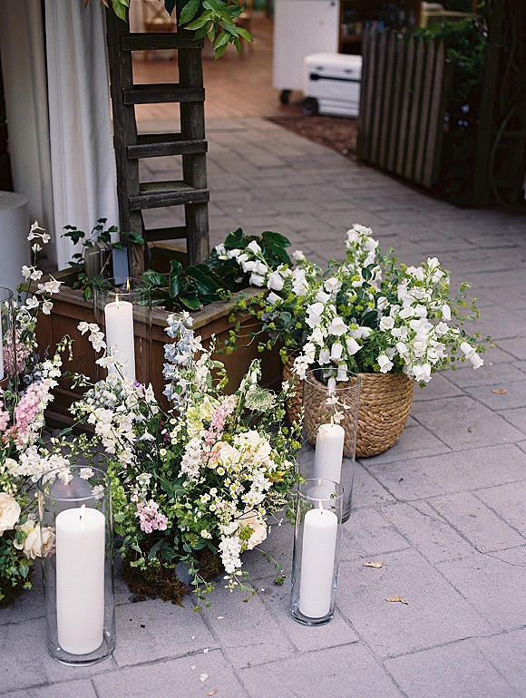 Wedding floral decor with outdoor wedding entry decor, white pillar candles in glass hurricane vases and wildflower greenery on stone pavers near entrance