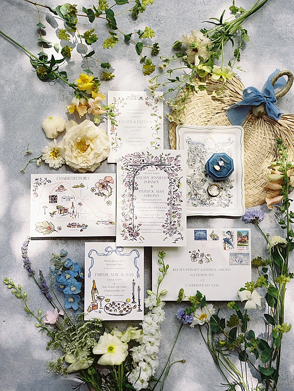Invitation suite wedding invitation flat lay with floral cards, map, stamped envelope, rings and blue ribbon on a gray stone surface