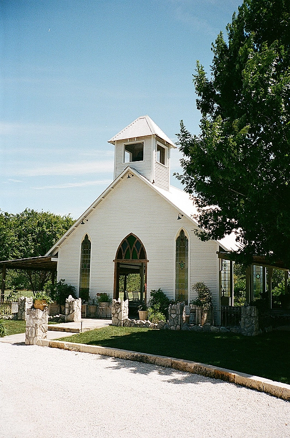 Chapel wedding venue with a small white chapel and stained glass windows, stone pillar porch and metal roof under a blue sky