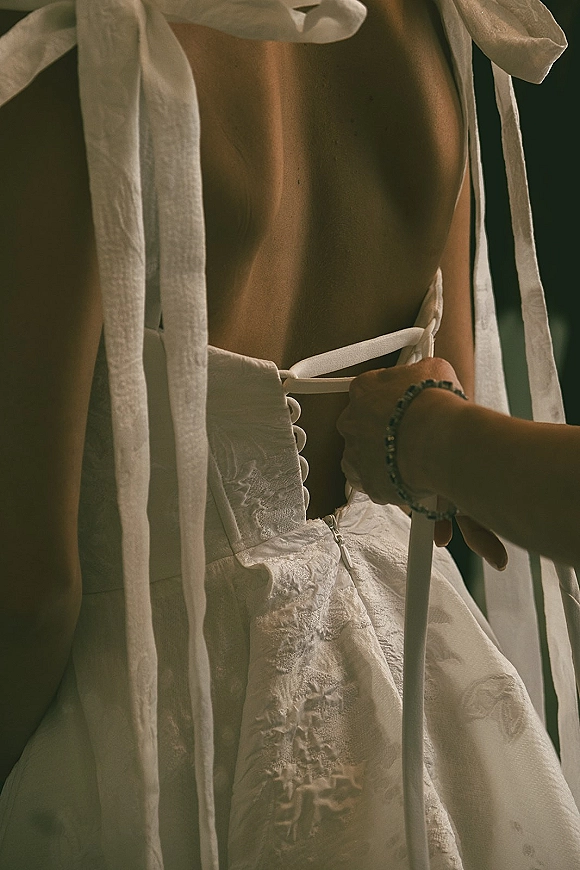 Wedding dress details showing a corset back wedding dress with lace bodice, ribbon ties, and bracelet in soft window-lit room
