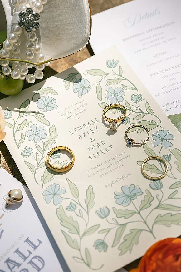 Wedding invitation suite with botanical wedding invitations, rings and pearl bracelet on a sunlit stone surface with greenery shadows
