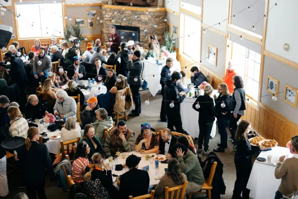 Wedding reception with guests mingling under string lights, gathered around white linen cocktail tables in a wood-paneled hall with stone fireplace