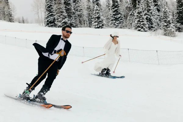 Skiing couple portrait of bride in a wedding dress and groom in a tuxedo on skis with a fur wrap on a snowy slope with pine trees