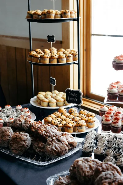 Wedding dessert table with a wedding cupcake display on tiered stands, mini muffins and chalkboard labels by a window in natural light