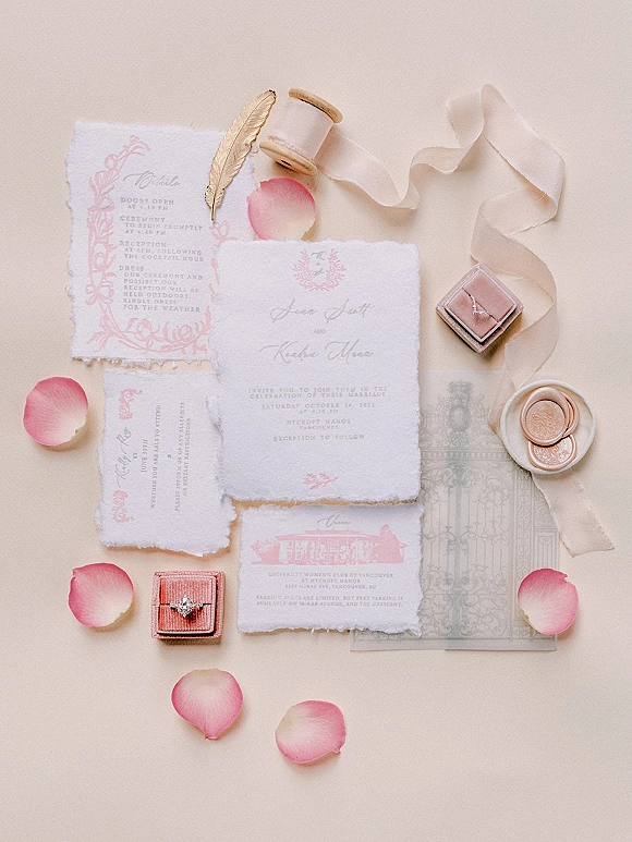 Invitation suite wedding invitation flat lay with deckle edge paper, blush calligraphy, silk ribbon spool, wax seal, ring box and pink petals on neutral tabletop