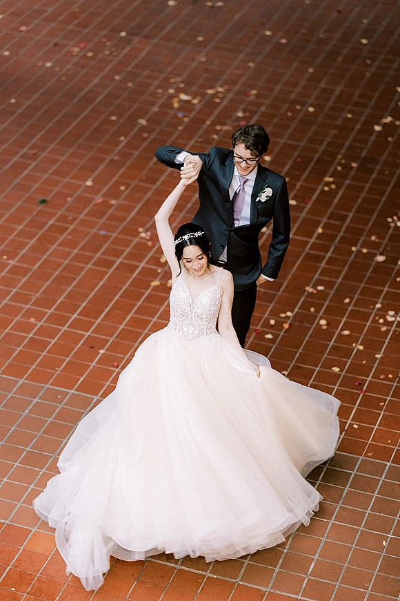 Wedding couple portrait from above, groom leading bride in a twirl as her tulle gown spreads on a brick tile floor with confetti