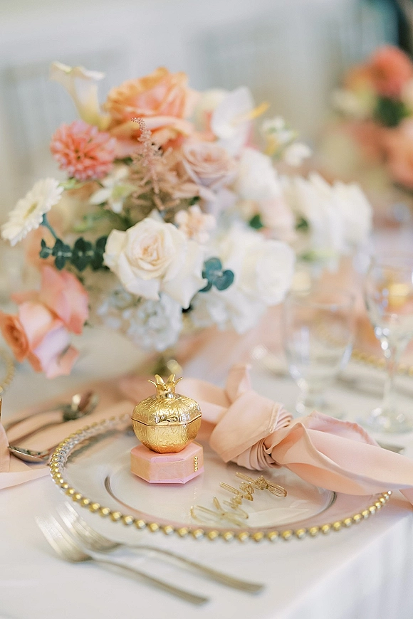 Reception tablescape with blush wedding tablescape details, rose and eucalyptus centerpiece, gold beaded charger, blush napkin, and favor box on white linen