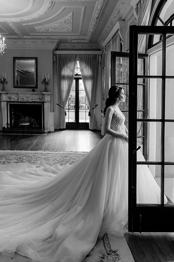 Bridal portrait of a bride by window in a strapless lace bodice and tulle skirt, long train spread in an ornate room with French doors