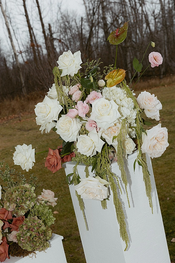 Wedding floral arrangement of white and blush roses with hydrangea on pedestal stands, set on a grass lawn beneath an overcast sky