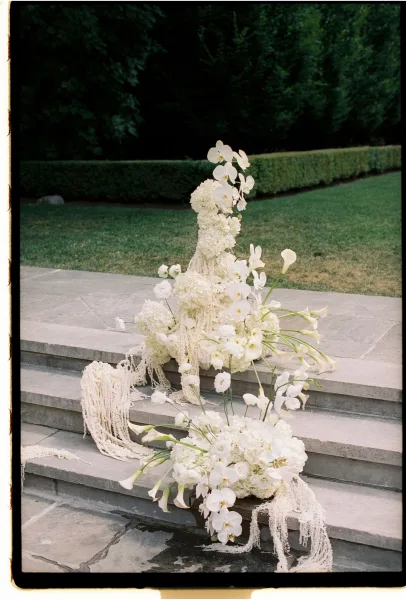Ceremony floral arrangement with wedding aisle flowers of white orchids, calla lilies, hydrangeas and hanging amaranthus on stone steps outdoors