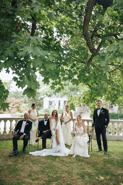 Wedding party portrait with bride in strapless gown and long veil seated with calla lily bouquet, bridesmaids and tuxedoed groomsmen on garden terrace