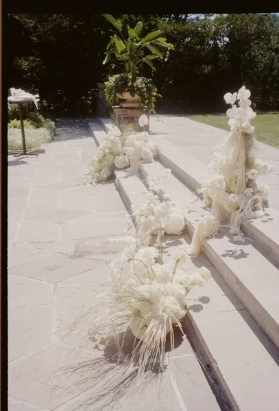 Ceremony aisle decor with outdoor ceremony aisle flowers, white orchid clusters and greenery lining stone steps in a garden setting