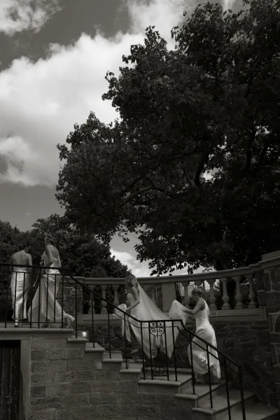 Bridesmaids portrait of the bridal party walking upstairs, helping the bride with her veil on a stone staircase with wrought iron railing