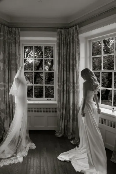 Bridal portrait of a bride looking out window in a strapless wedding dress with cathedral lace veil, heels and perfume on the windowsill