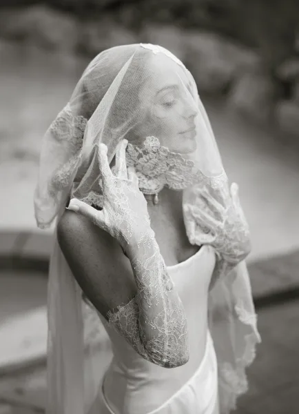 Bridal portrait in black and white of a bride with veil over face, lace gloves and pearl necklace on outdoor stone steps