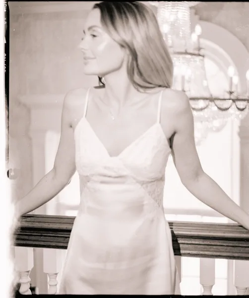 Bridal portrait in black and white of bride leaning on an interior balcony railing, looking away in a lace bodice satin dress under a chandelier