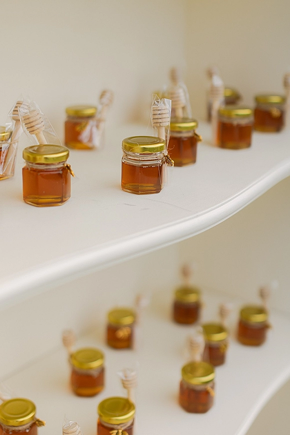 Wedding favors honey jar wedding favors with gold lids and honey dippers, wrapped in cellophane with twine on a white tiered shelf