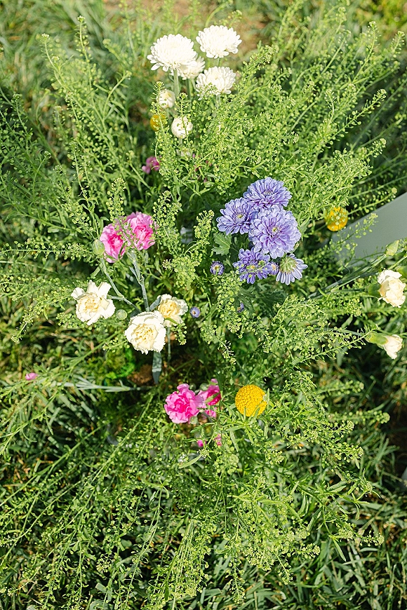Wedding florals with wildflower wedding flowers in a loose garden arrangement of white blooms, purple and pink stems, yellow billy balls on grass