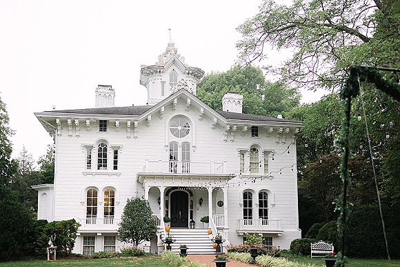 Wedding venue exterior of a white wedding venue with string lights and hanging bulbs over the porch, wreath and lanterns by front steps amid gardens