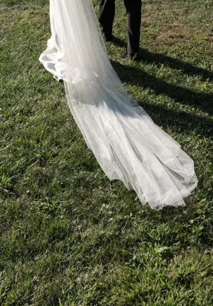 Wedding dress train with tulle wedding dress train trailing on sunlit grass as bride and groom walk away, their shadows stretching behind