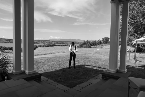 Groom portrait with groom getting ready vibe, adjusting suspenders over a white shirt on a porch with columns and rolling hills behind