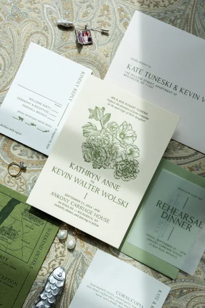 Invitation suite wedding invitation flat lay with envelopes, RSVP and map cards, rings, pearl earrings, cufflinks, and wax seal on patterned fabric