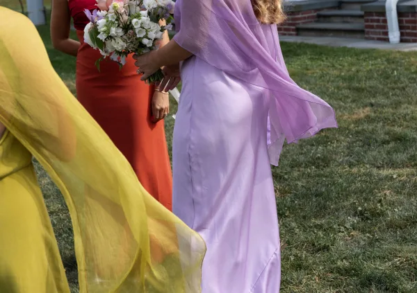 Bridesmaid dresses in lavender, yellow, and rust with chiffon wraps, holding white bouquets on brick steps by a grassy lawn outdoors