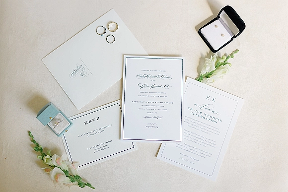 Wedding invitation suite with classic wedding invitations, RSVP card, rings and pearl earrings styled on linen with floral accents
