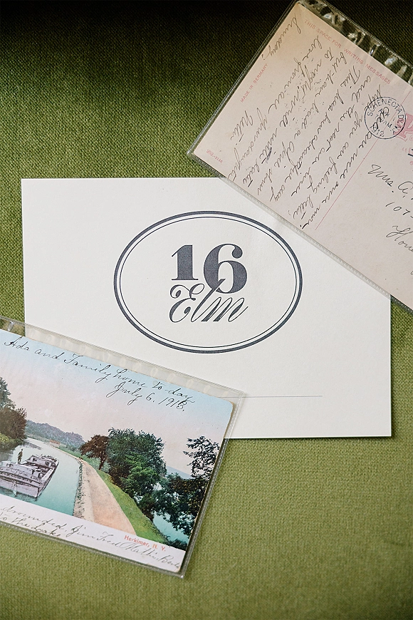 Wedding table number 16 card with oval border and classic typography, styled with vintage postcards in plastic sleeves on green linen fabric