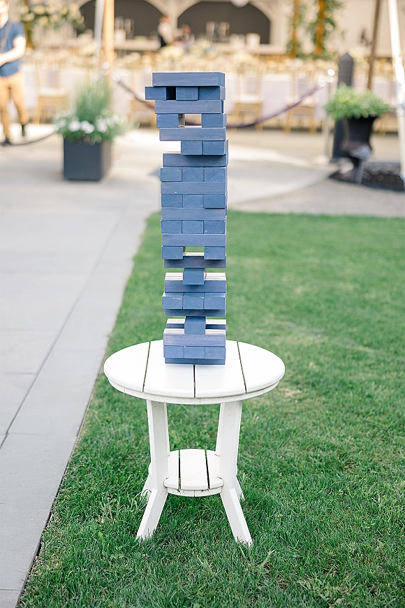 Giant jenga game set for wedding lawn games with blue wooden blocks beside a white side table on a grassy reception area