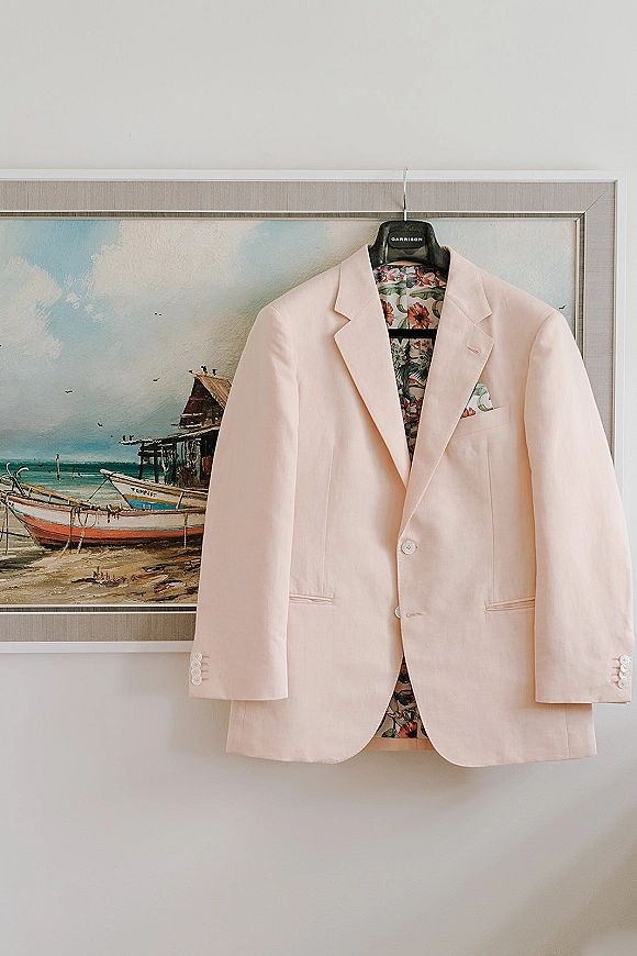 Groom suit jacket on hanger with floral lining and patterned pocket square, framed wall art in the background and button details