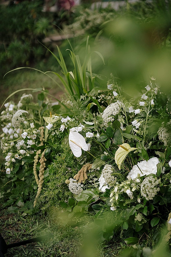 Wedding floral arrangement with grounded ceremony flowers in white blooms and greenery, featuring anthurium amid garden grass and foliage