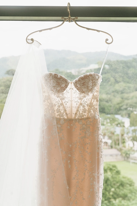 Wedding dress hanging in a window, a strapless lace wedding dress with veil on a decorative hanger against a mountain view