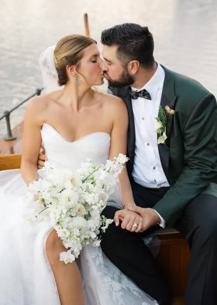 Wedding kiss portrait of bride and groom kissing on a boat deck by the water, bride holding a white bridal bouquet with veil flowing