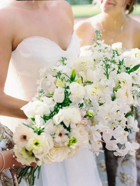 Bridesmaid bouquet of white bridesmaid bouquets with lush greenery, held by women in strapless dresses in sunlit outdoor greenery