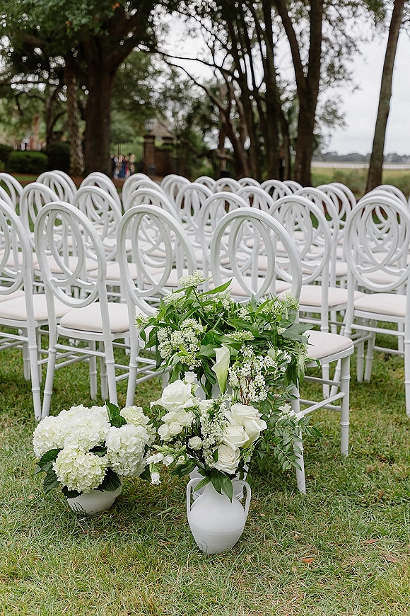 Ceremony seating with outdoor wedding ceremony chairs in neat rows, lined with white rose and hydrangea florals and greenery on a garden lawn
