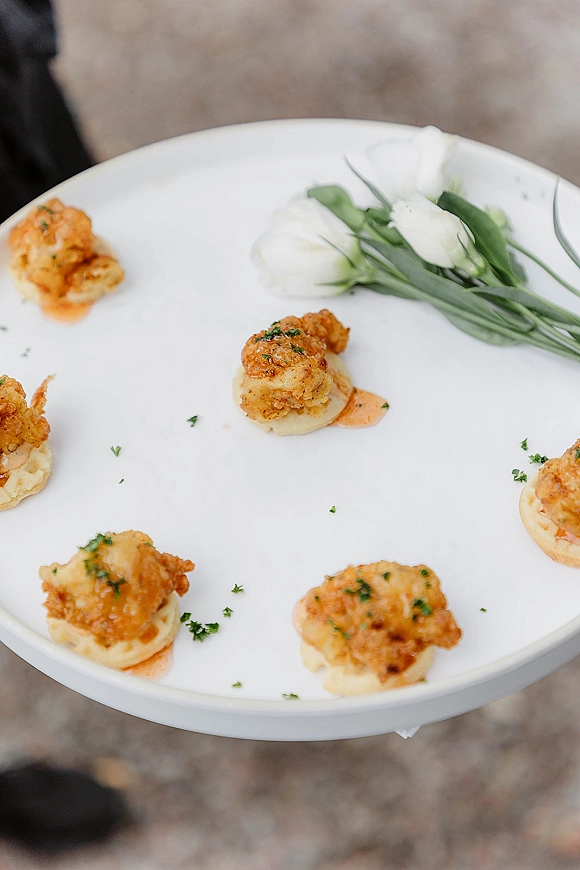 Wedding hors d'oeuvres on a passed appetizer plate with fried shrimp bites over creamy base, herb garnish and dipping sauce on a white plate