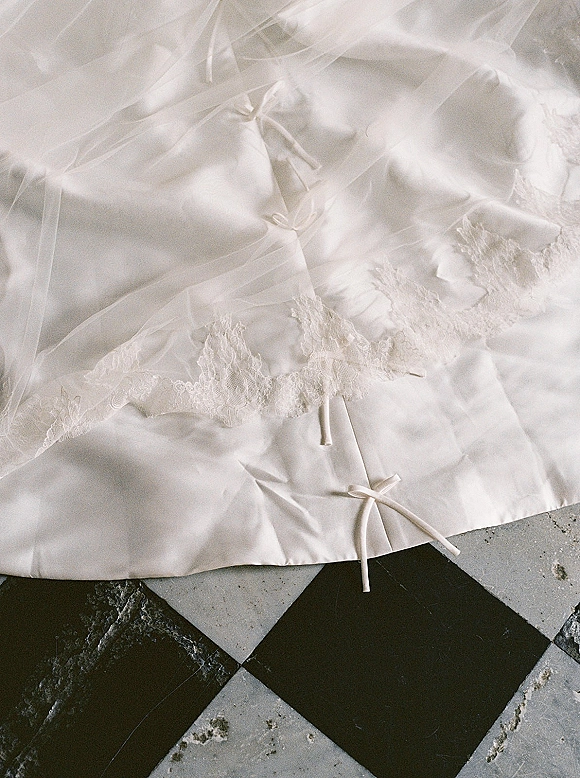 Wedding dress detail showing bridal gown lace trim and ribbon ties with tulle layers resting on a black and white checkered tile floor