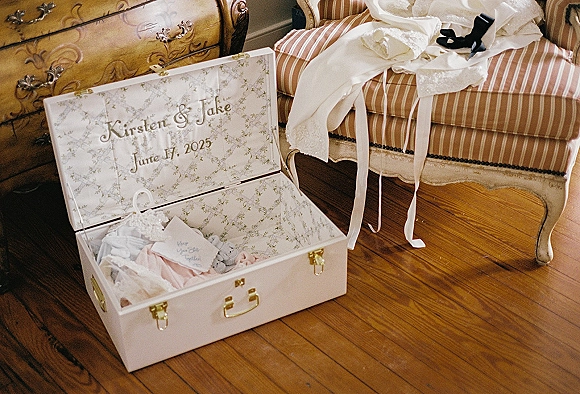 Wedding keepsake box with floral lining and handwritten note beside lace ribbon and wedding shoes on a striped chair by an antique dresser