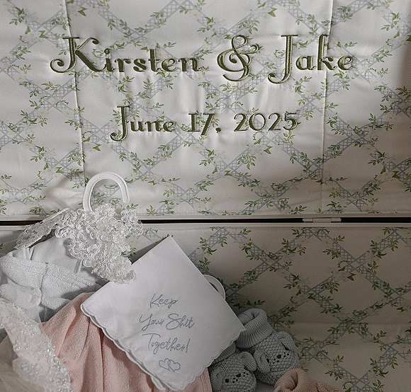 Wedding dress detail with lace wedding dress beading on a hanger beside an embroidered wedding date handkerchief on floral fabric