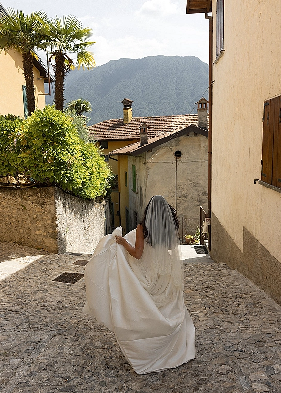 Bridal portrait of bride walking away in a strapless wedding dress with cathedral veil, holding her train on a cobblestone old town street