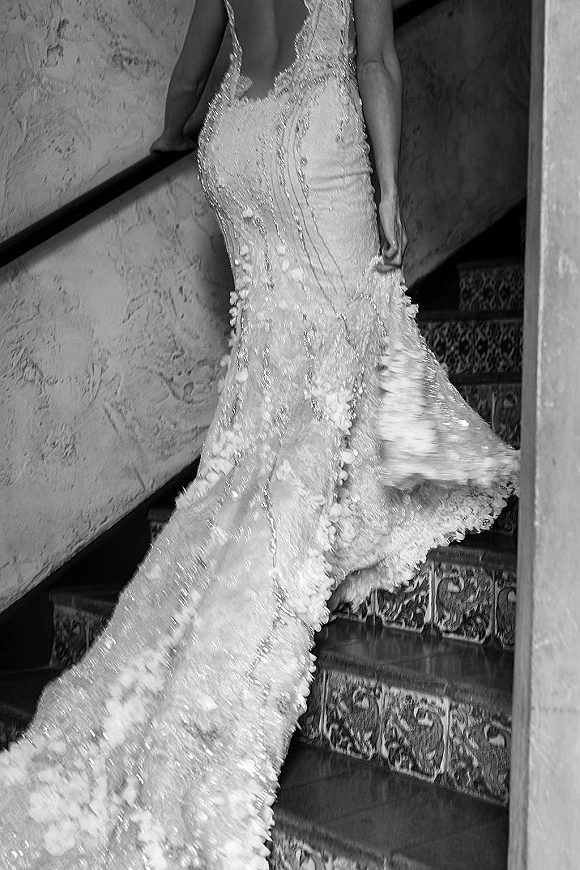 Wedding dress close-up of a beaded wedding dress with lace appliques and a long train cascading over tiled staircase steps